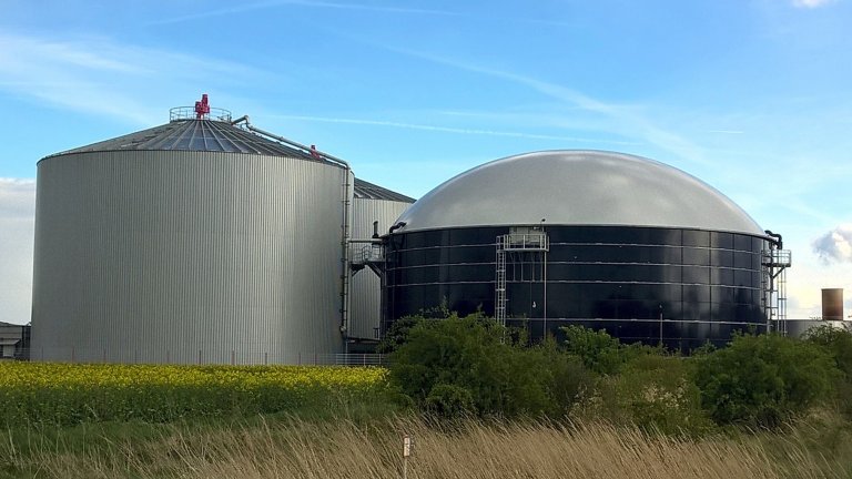 Biogasbehälter hinter Wiese unter blauem Himmel Biogasbehälter hinter Wiese unter blauem Himmel